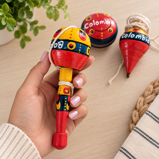 Hand holding a hand-painted Colombian coca cup-and-ball toy with yoyo and trompo behind it