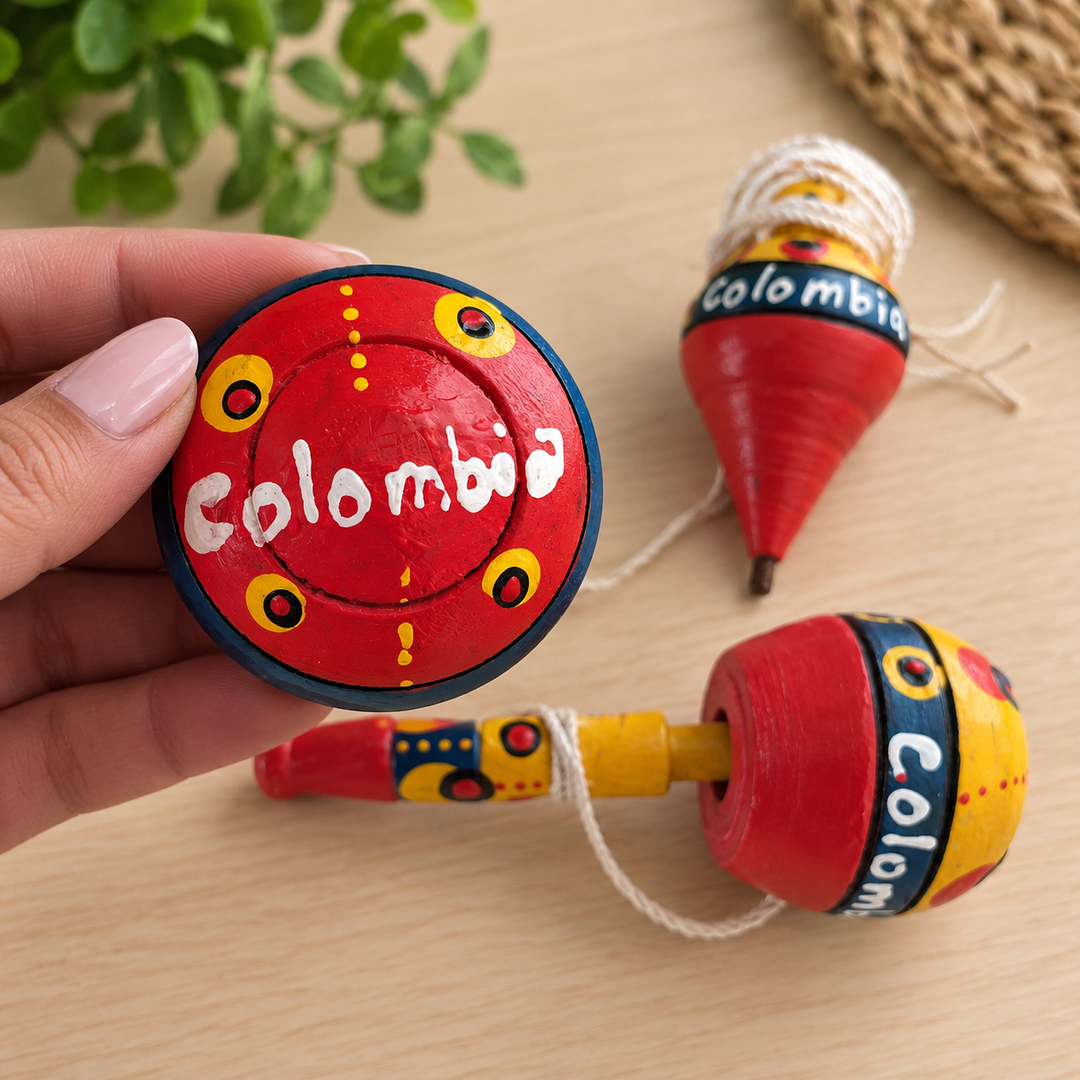 Hand holding a hand-painted Colombian yoyo with traditional coca and trompo in the background