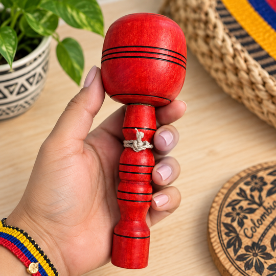 Hand holding a traditional Colombian red coca wooden cup-and-ball toy